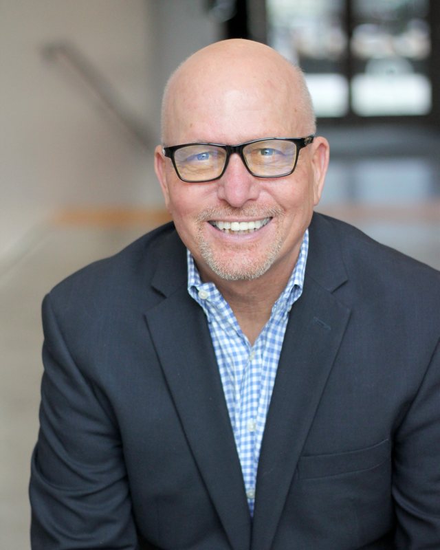 Portrait of Tim Winner, smiling, in glasses and a navy blazer